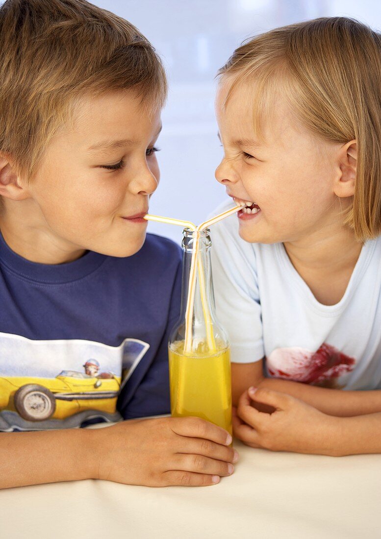 Kinder trinken Orangenlimonade mit Strohalm