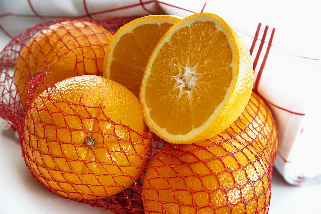 Orangen in geöffnetem Netz, eine halbiert