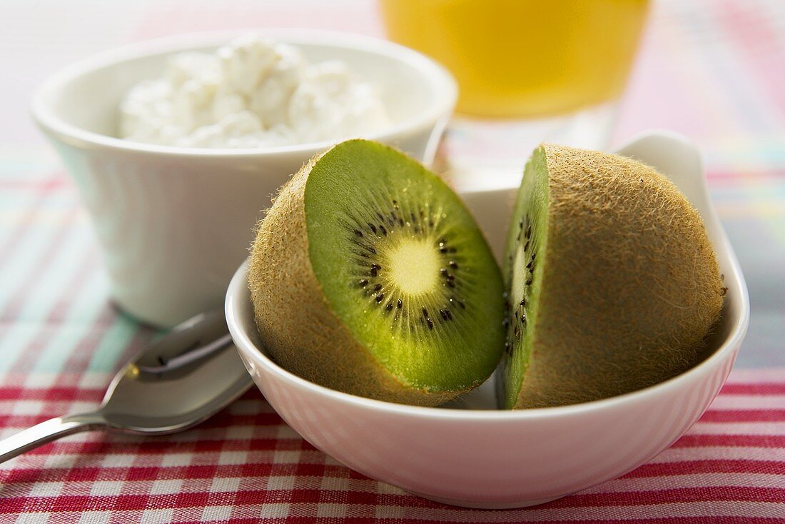 Halved kiwi fruit in front of a small bowl of cottage cheese