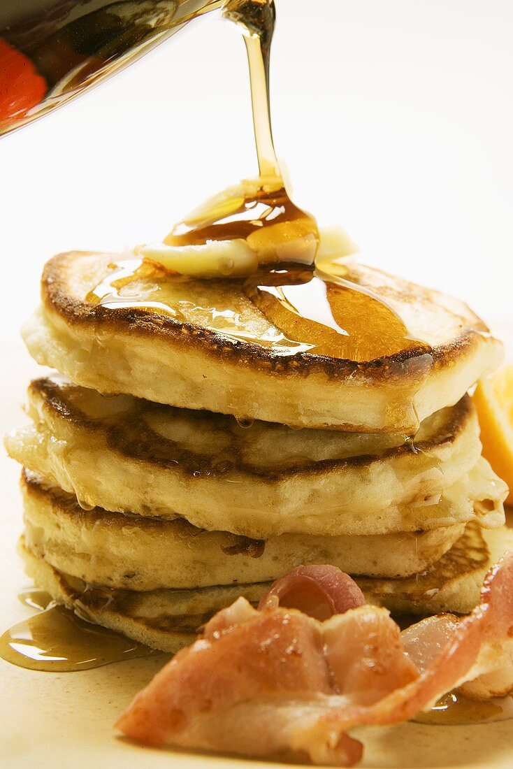 Pouring maple syrup over pancakes, butter and bacon