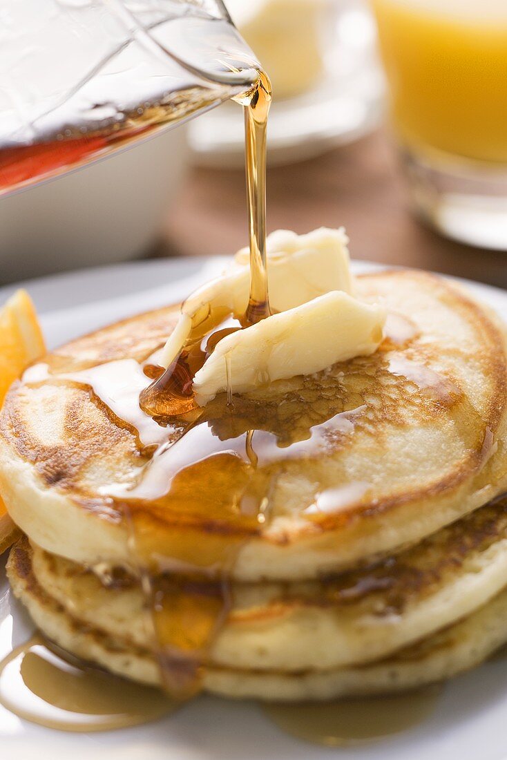 Pancakes und Butterflocke werden mit Ahornsirup begossen