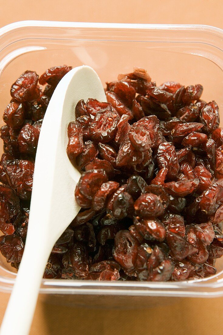 Dried cranberries with wooden spoon in plastic container