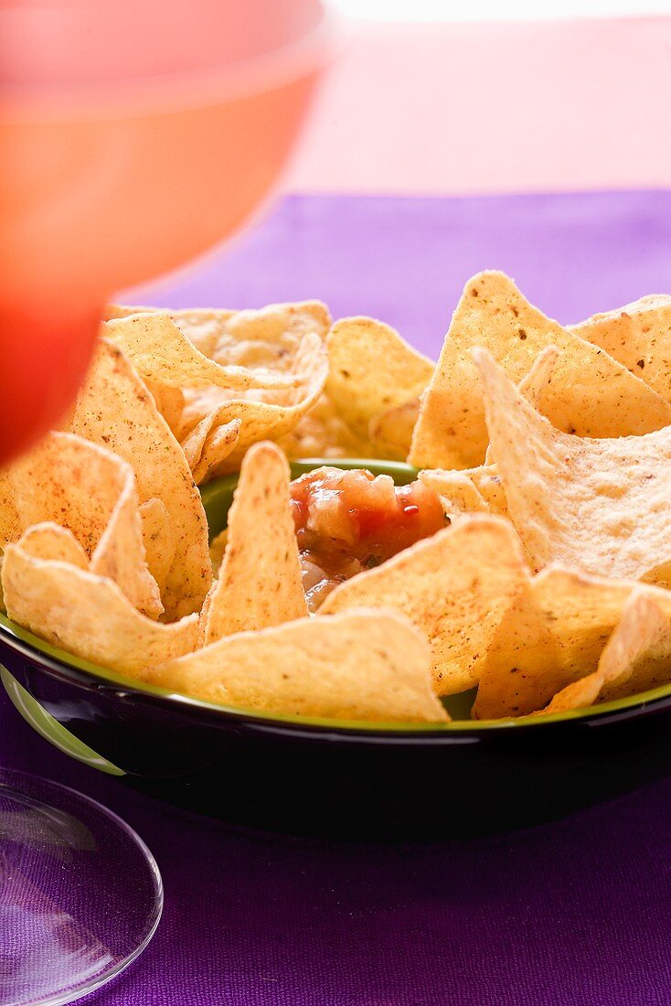 Tortilla chips and salsa in a bowl, cocktail beside it