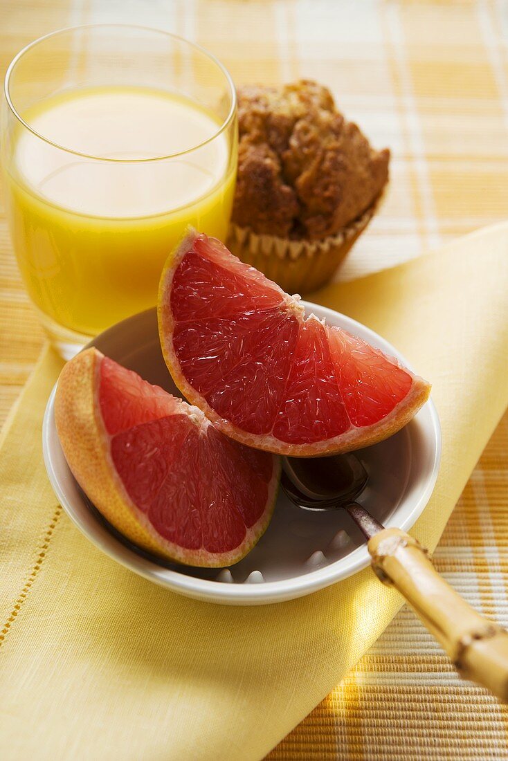 Grapefruit in a bowl, muffin and juice behind