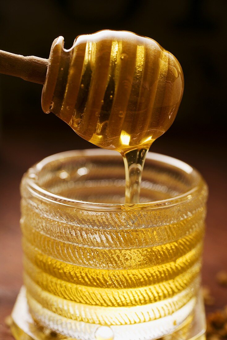 Honig fliesst von Honiglöffel in Honigglas