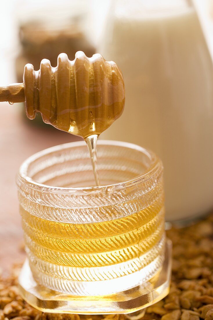 Honey running from honey dipper into honey jar, milk behind
