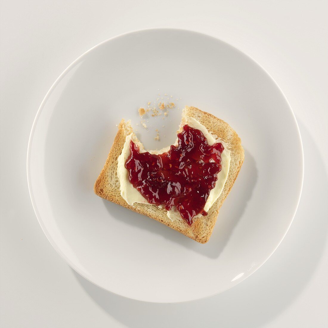 A slice of toast with butter and jam, a bite taken