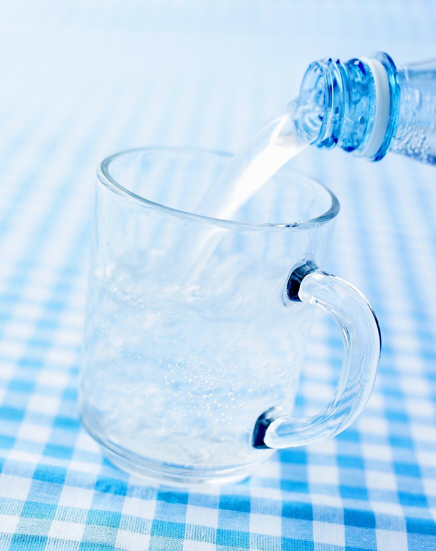 Pouring mineral water into a glass mug