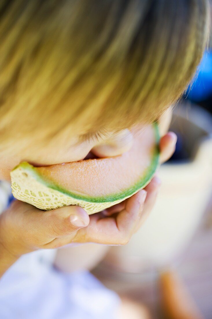 Small child biting into a slice of melon