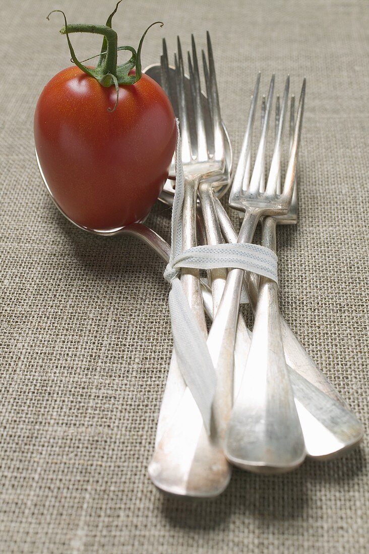 A tomato with forks and spoons