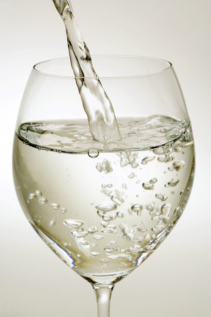 Mineralwasser in ein Weinglas eingiessen