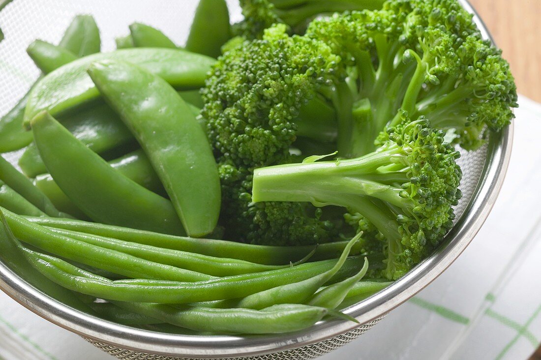 Cooked beans, mangetout and broccoli in a sieve