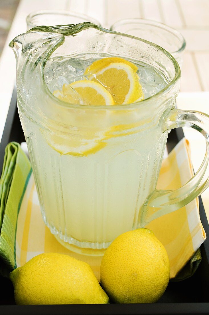 Lemonade in a glass jug with slices of lemon and ice