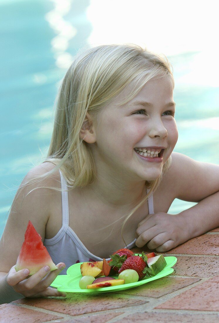 Kleines Mädchen mit frischen Früchten am Pool