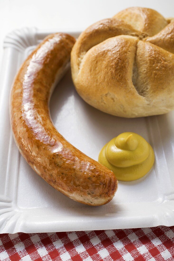 A sausage with mustard and bread roll on paper plate