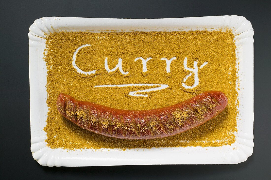 A currywurst in curry powder on a paper plate