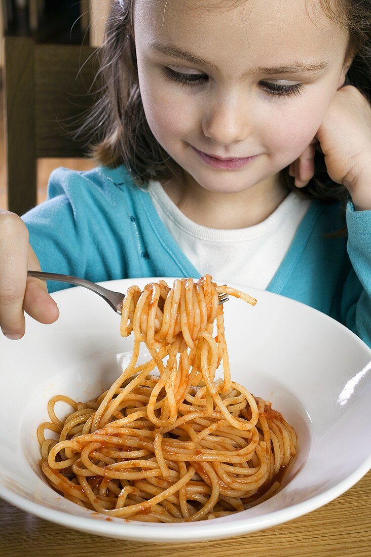 Small girl eating spaghetti with tomato sauce