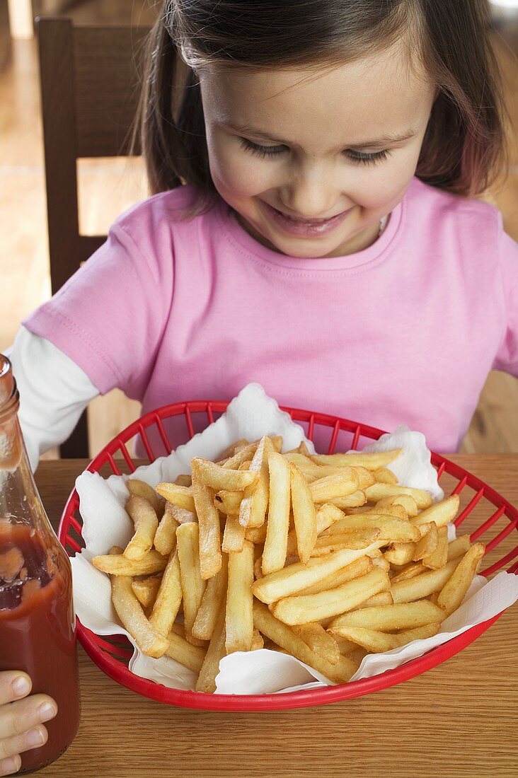 Small girl sitting in front of a basket of chips, ketchup