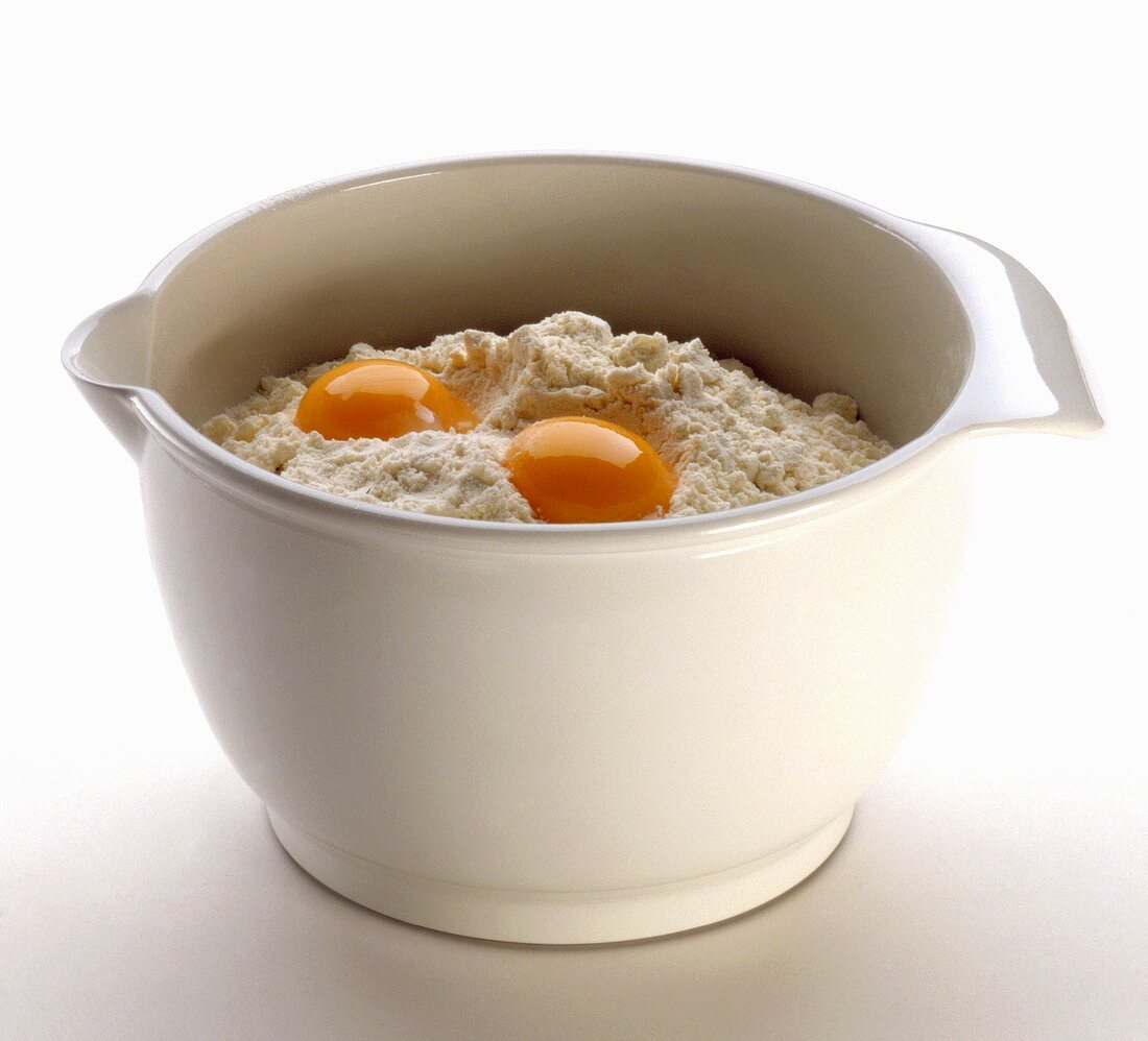 A bowl of flour with two eggs broken into it