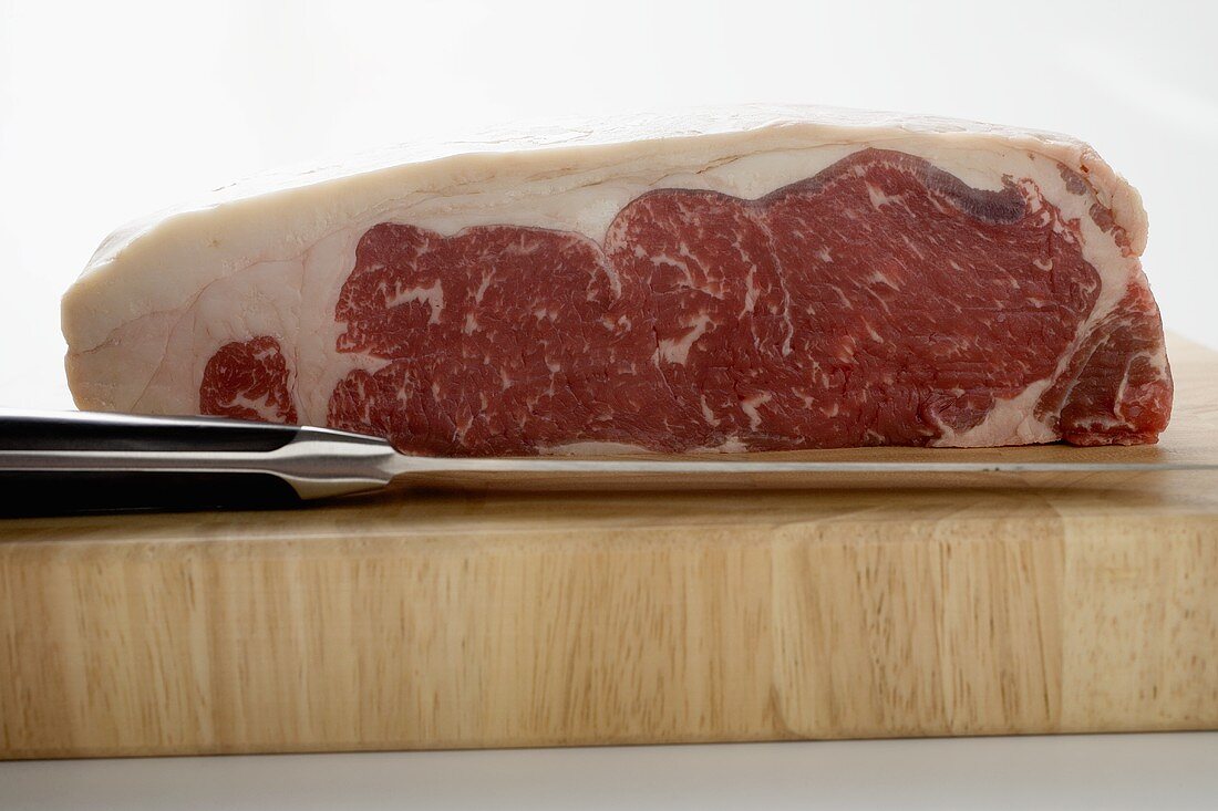 A piece of beef sirloin on wooden board with knife