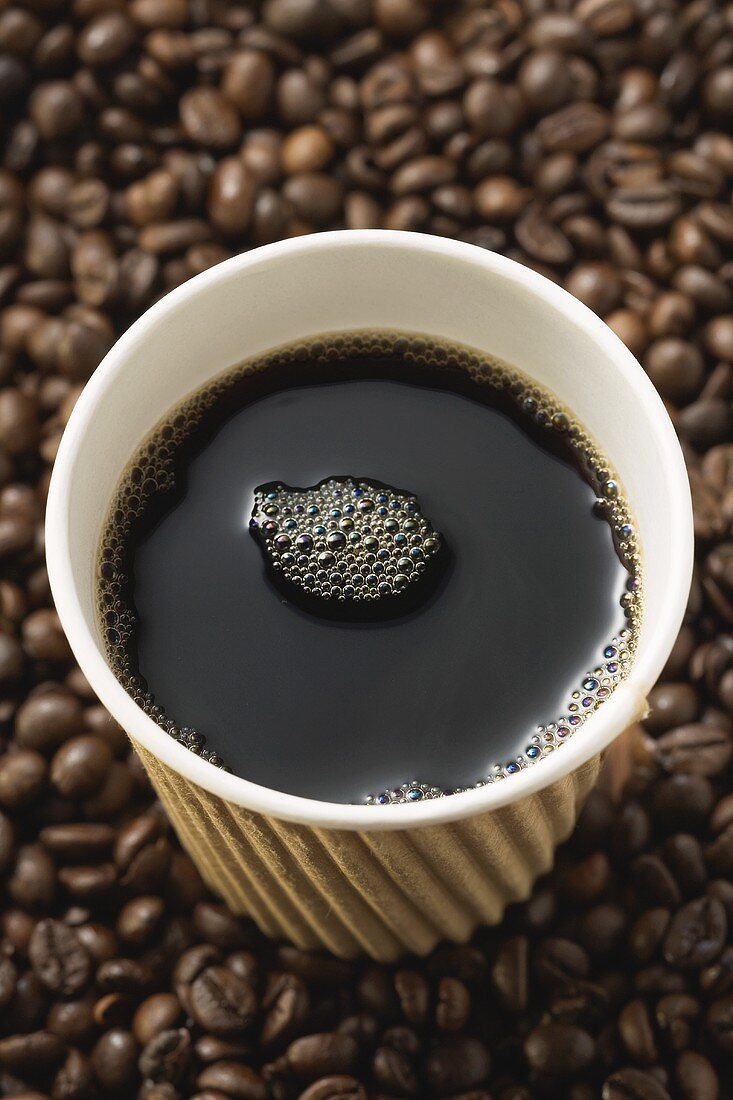 Ein Becher Kaffee steht auf Kaffeebohnen