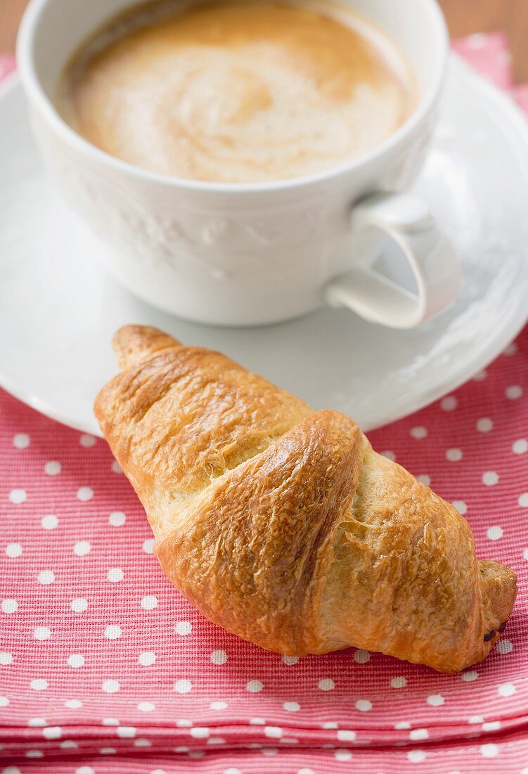 Ein Croissant zu einer Tasse Cappuccino