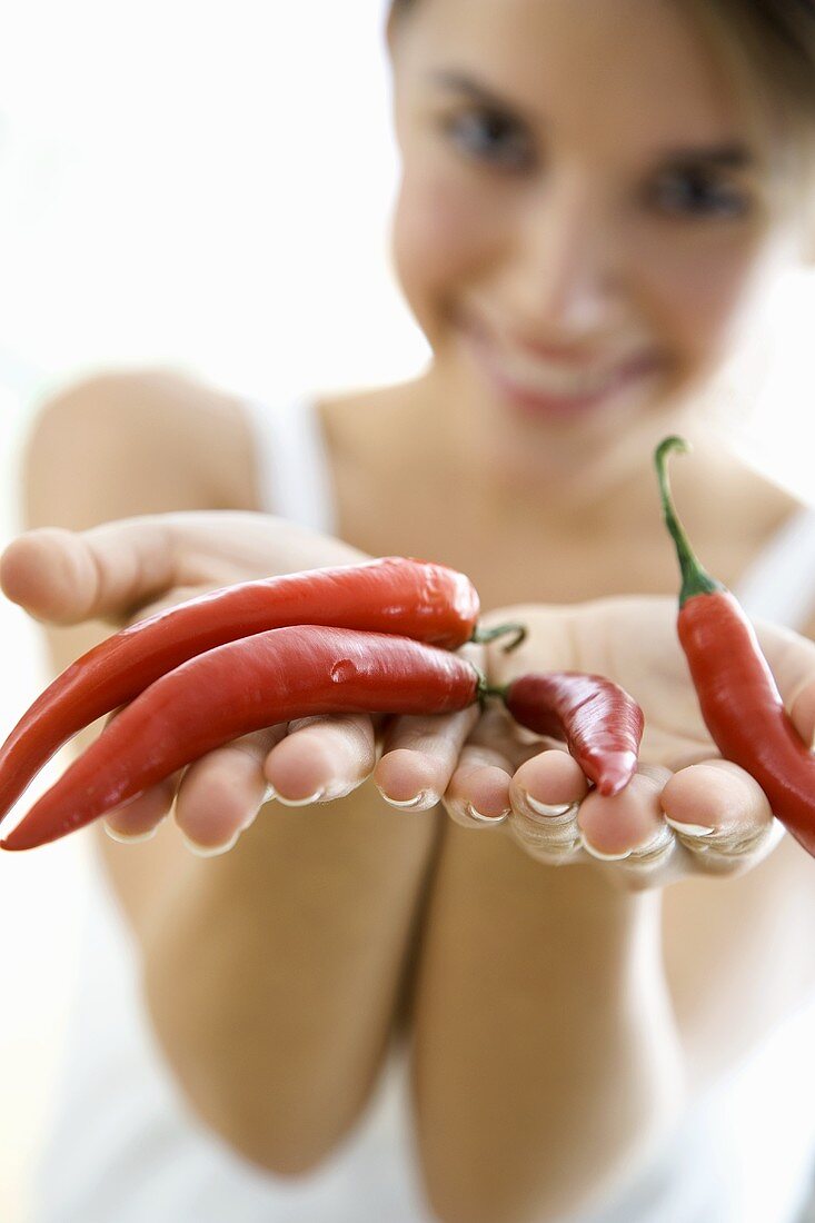 Young woman holding four red chillies in her hands