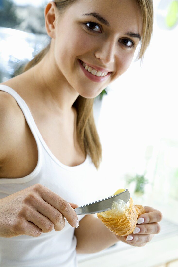 Junge Frau streicht Butter auf ein Croissant