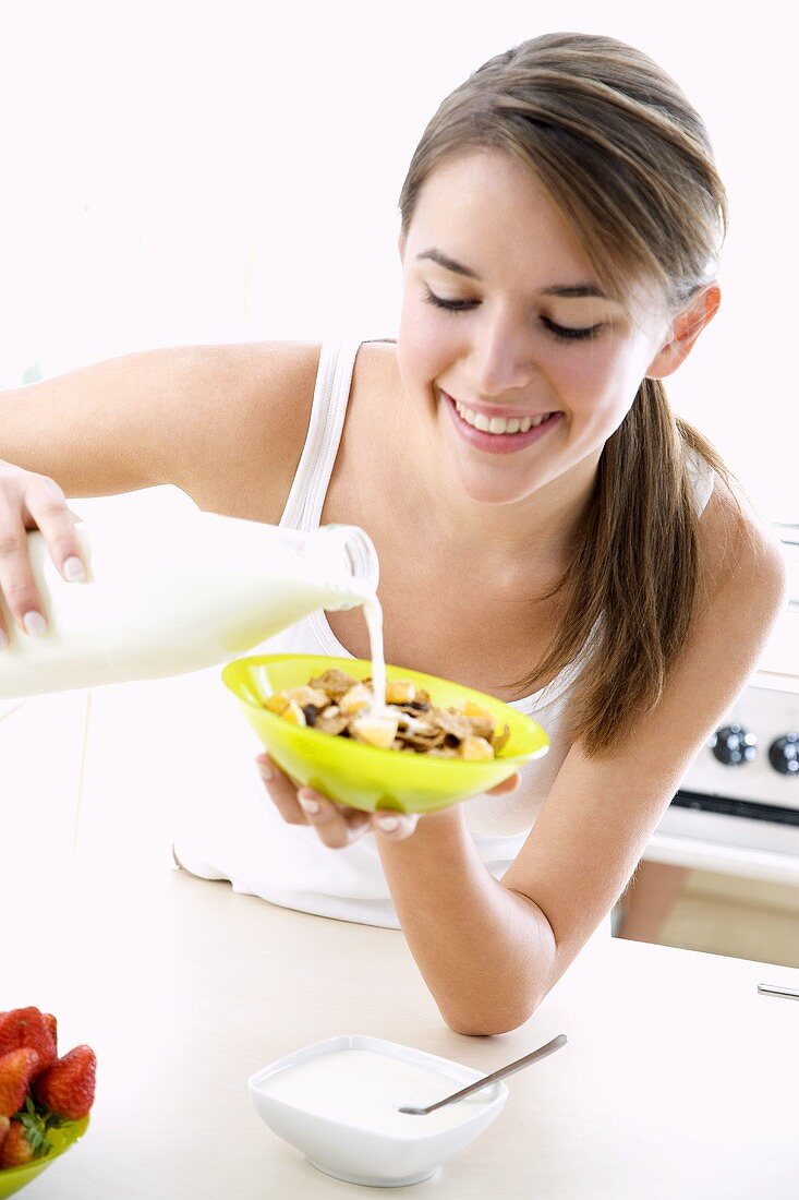 Junge Frau schüttet Milch in eine Schüssel Cornflakes