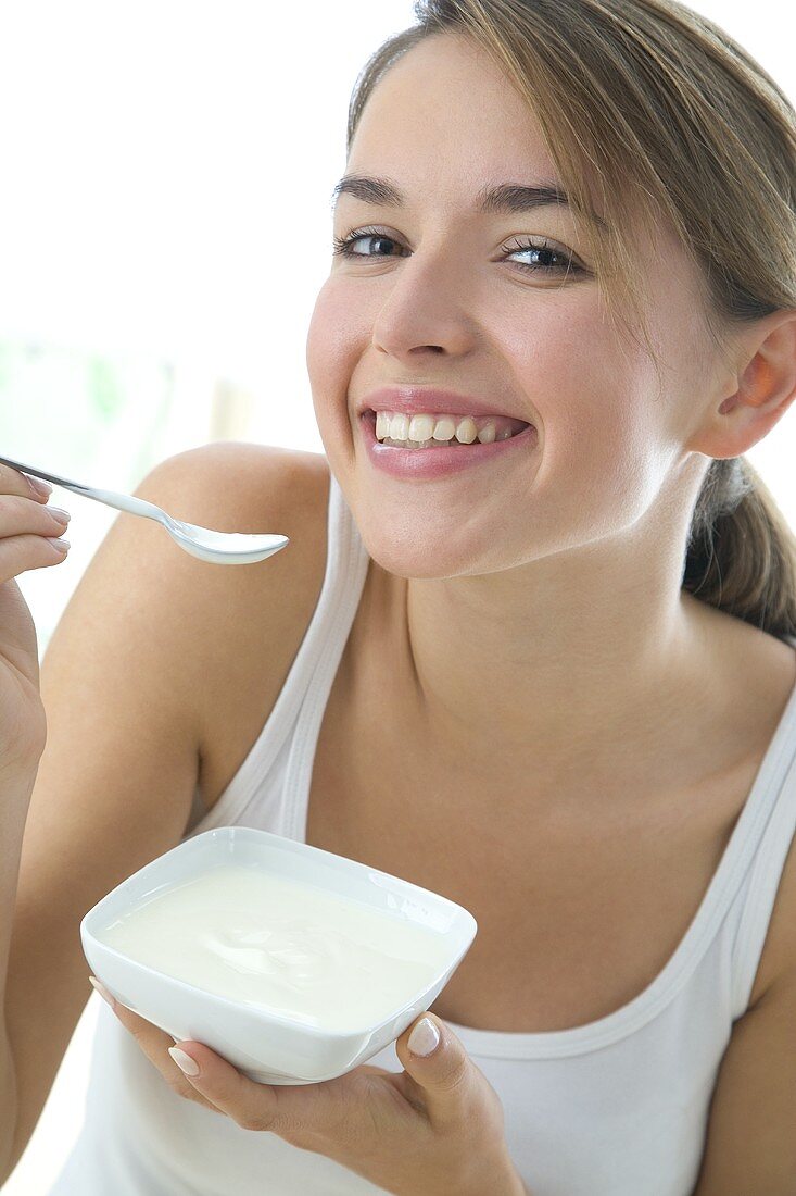 Young woman eating yoghurt out of a small bowl
