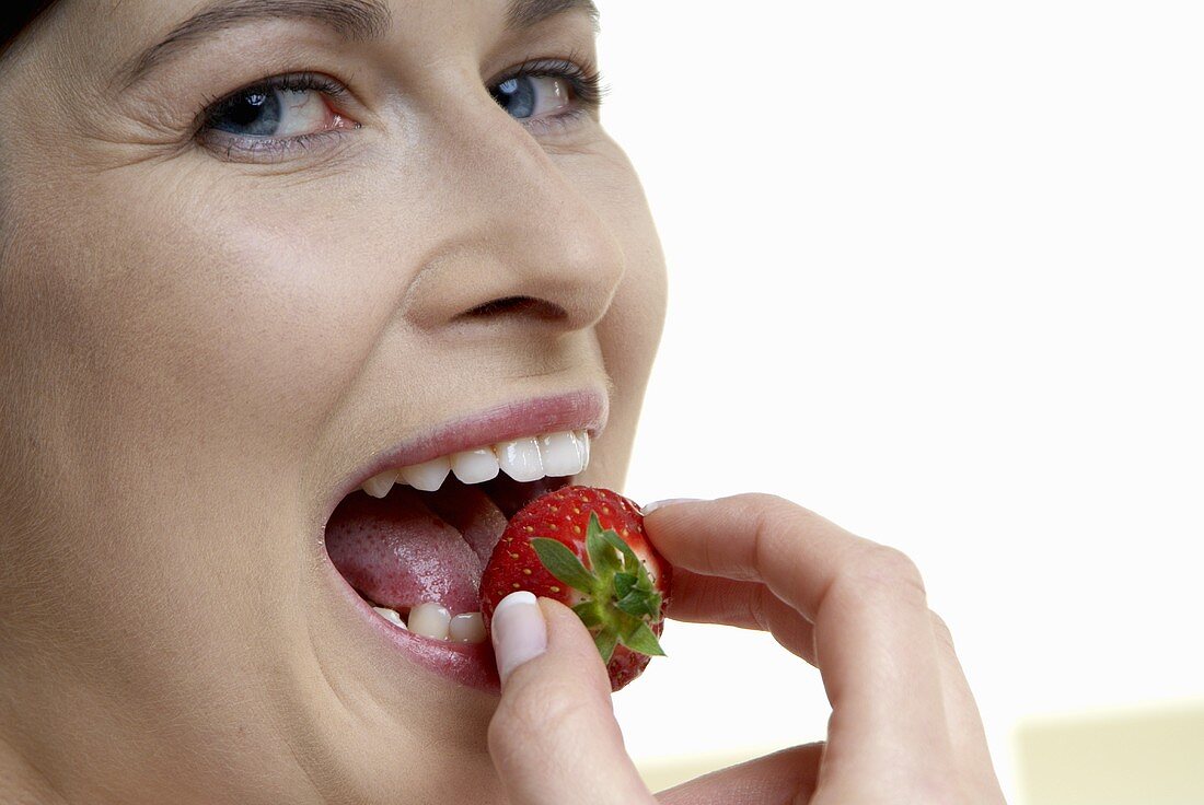Frau hält eine Erdbeere vor den Mund