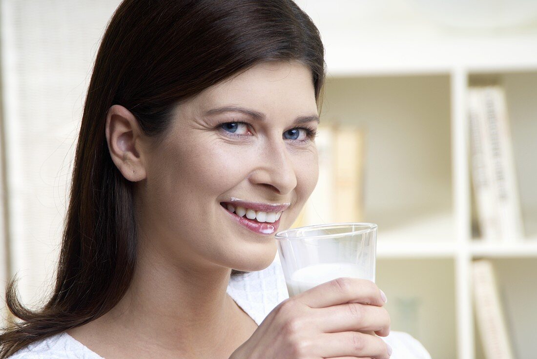 Woman with milk round mouth holding a glass of milk