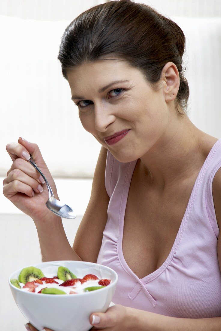 Woman eating yoghurt with kiwi fruit and strawberries