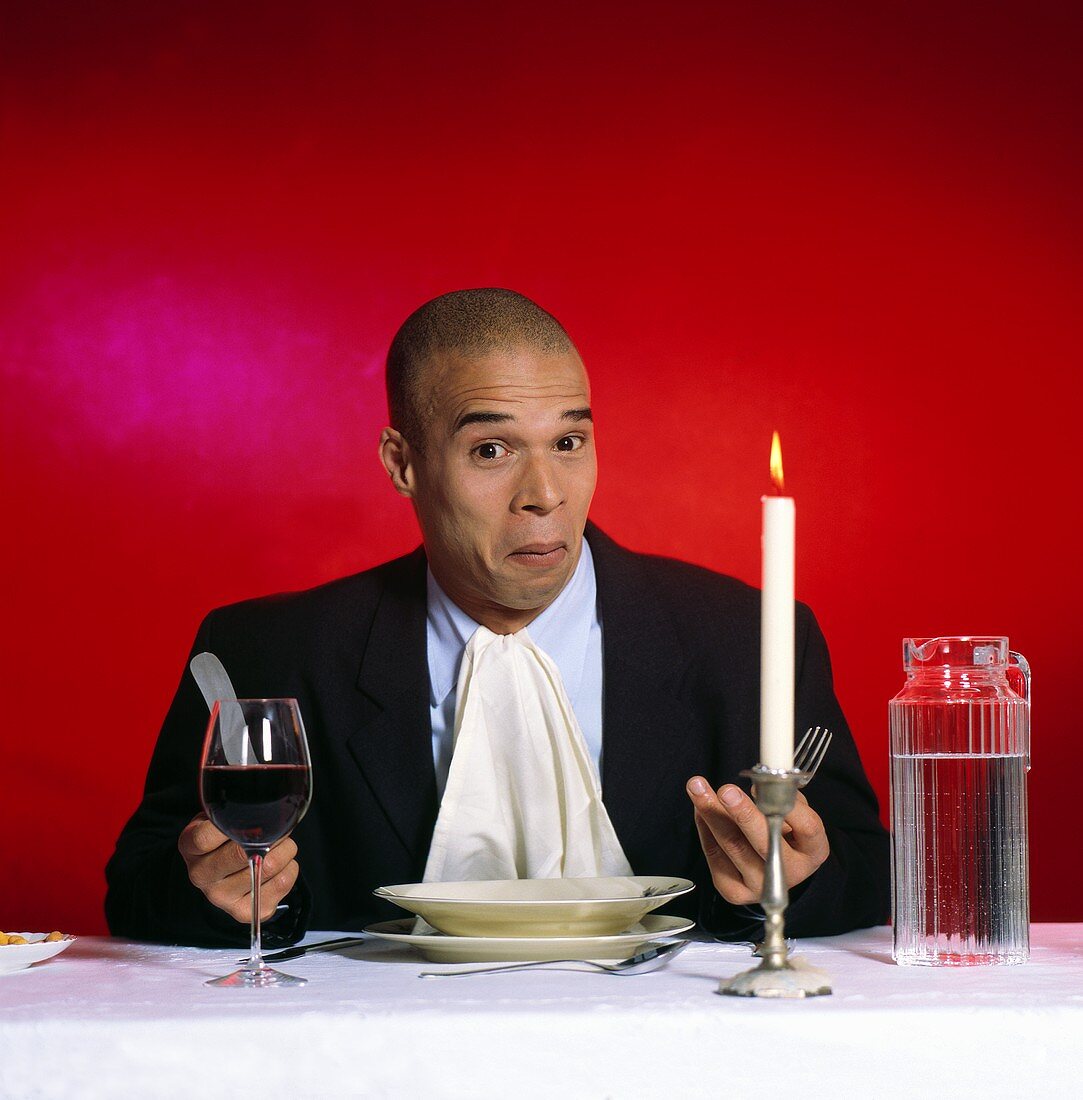 Mann sitzt vor leerem Teller mit Wasser und Wein