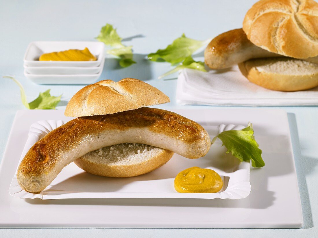 Two bread rolls filled with sausages on paper plates