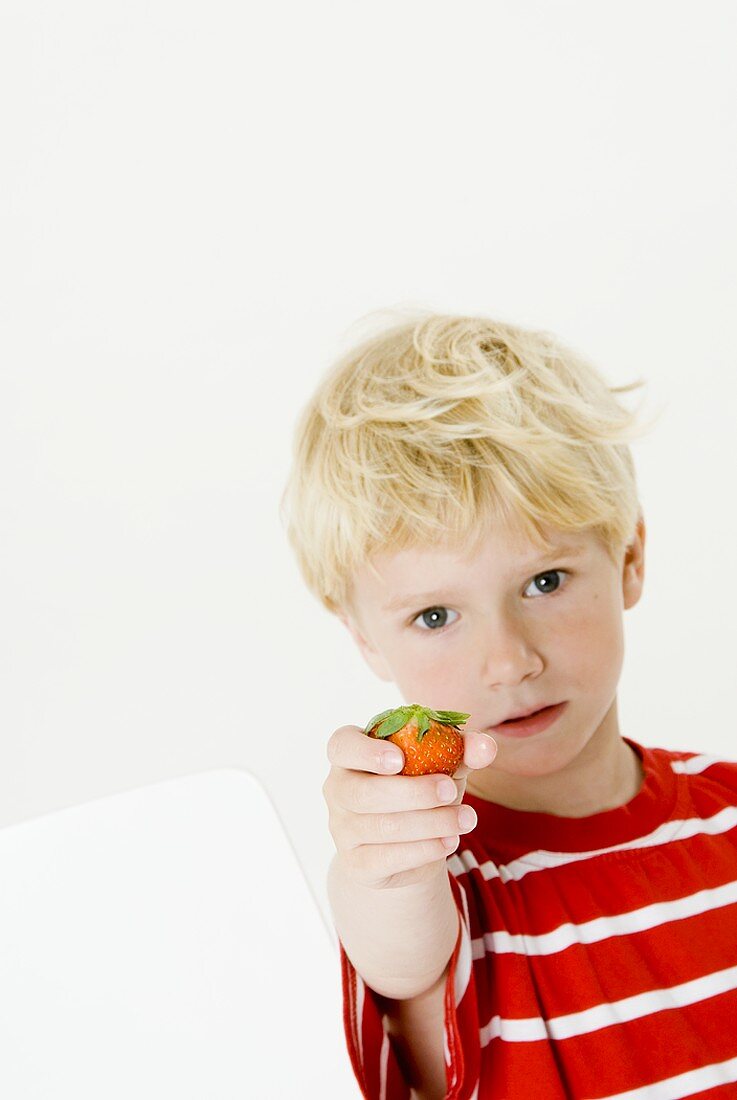Blond boy holding a strawberry in his hand