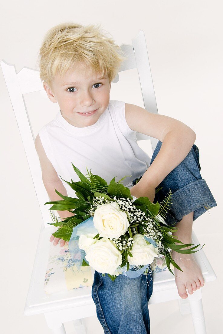 Junge mit weißem Rosenstrauss sitzt auf einem Stuhl