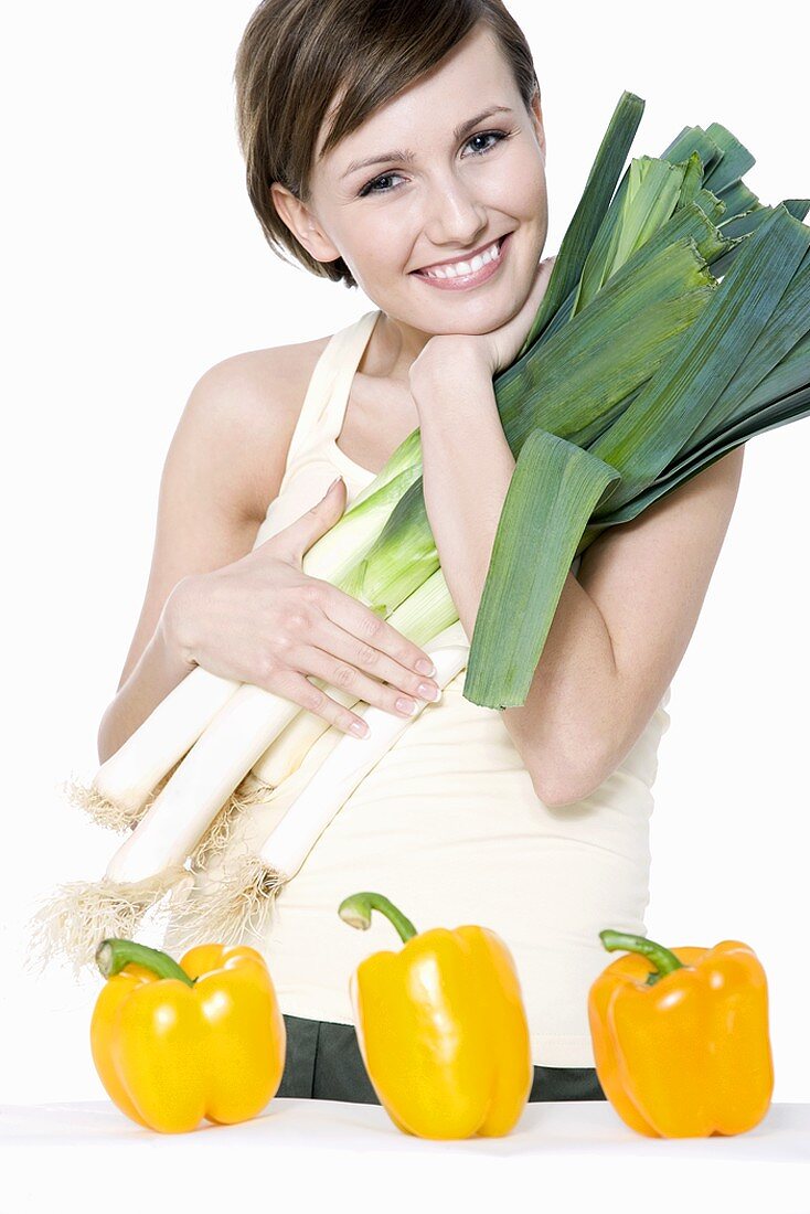 Young woman with fresh leeks, yellow peppers in front