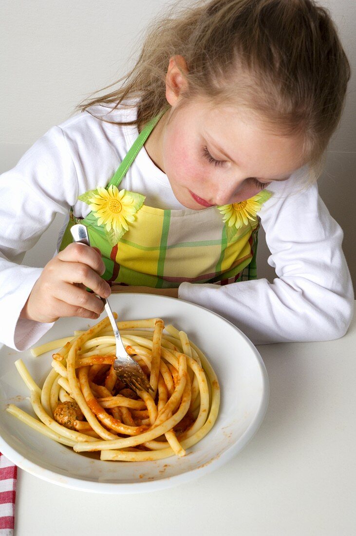 Young girl eating macaroni with tomato sauce