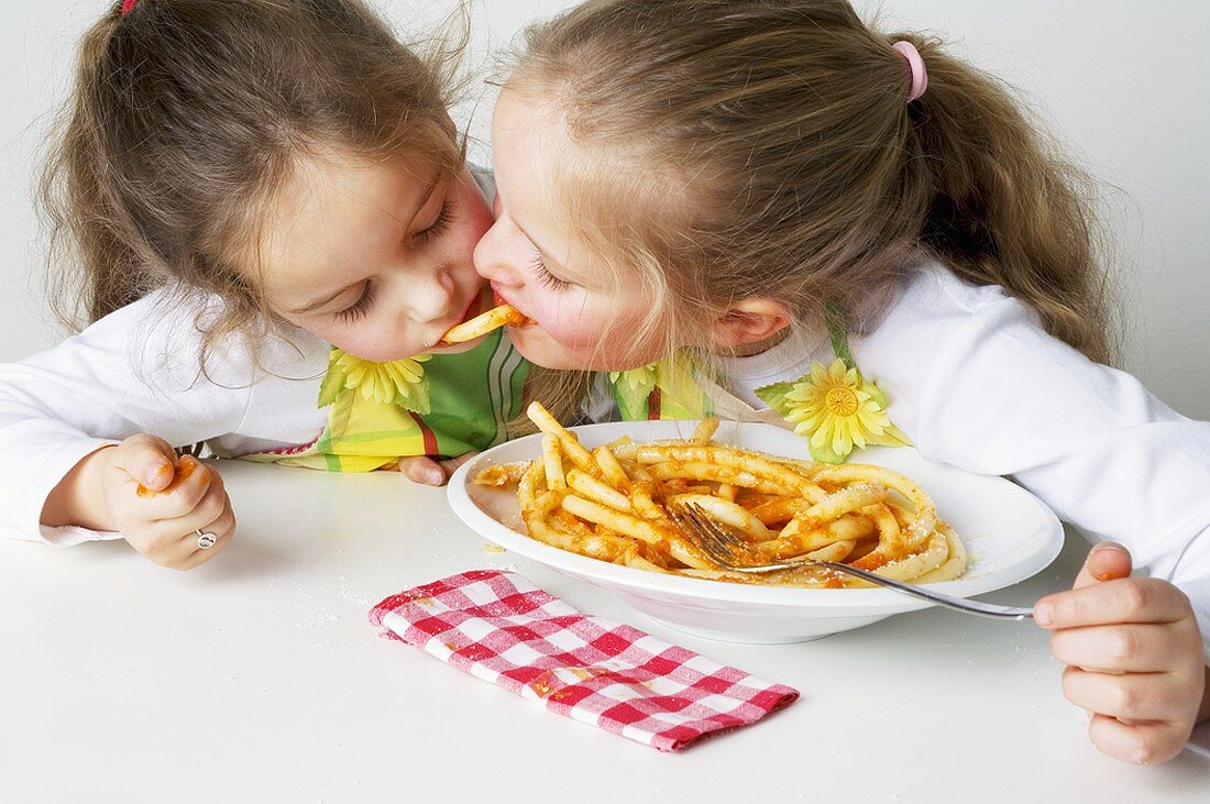 Two girls eating macaroni with tomato sauce