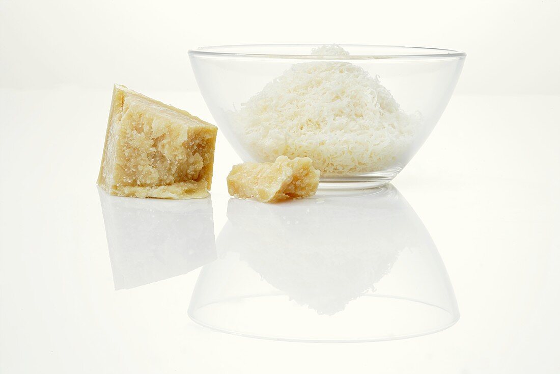 A piece of Parmesan and grated Parmesan in glass bowl