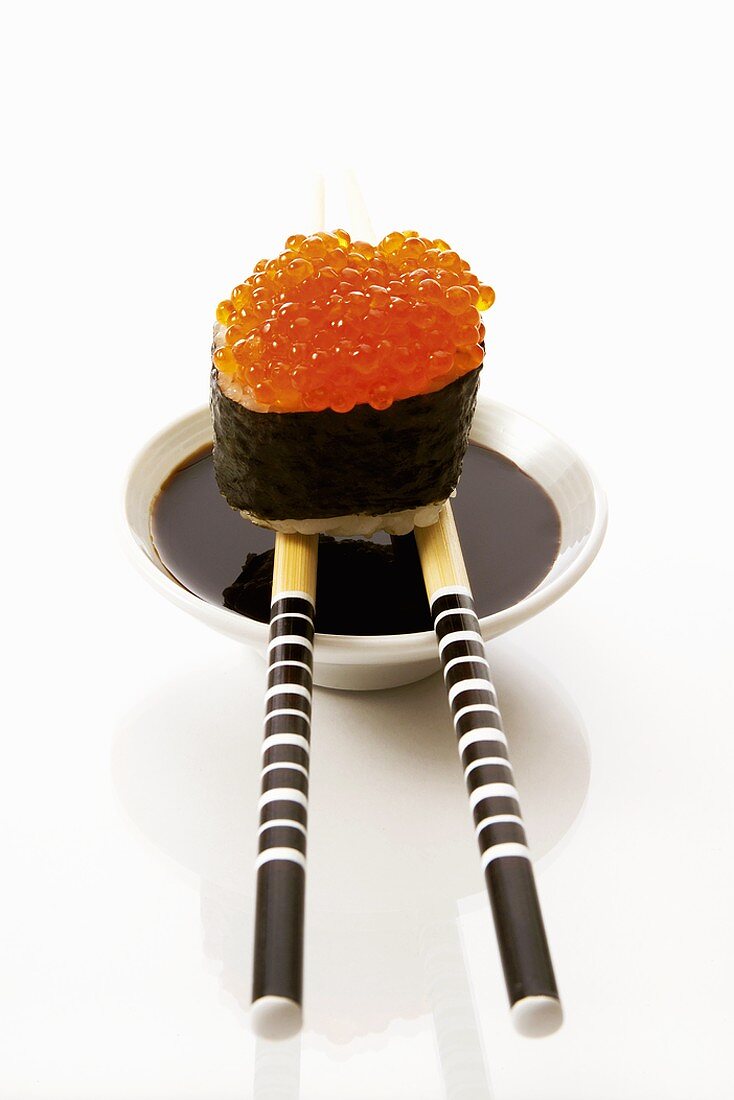 Gunkan maki on chopsticks on small bowl of soy sauce