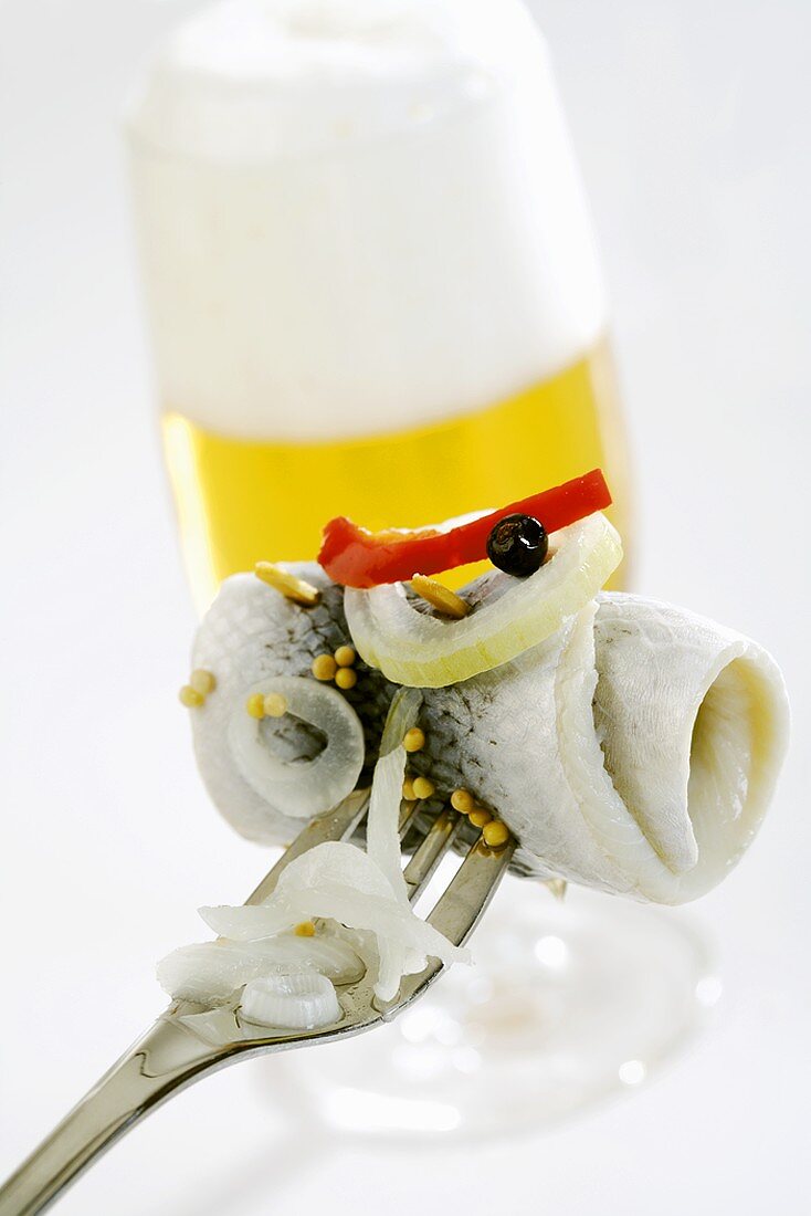 Ein aufgespiesster Rollmops mit Bier im Hintergrund