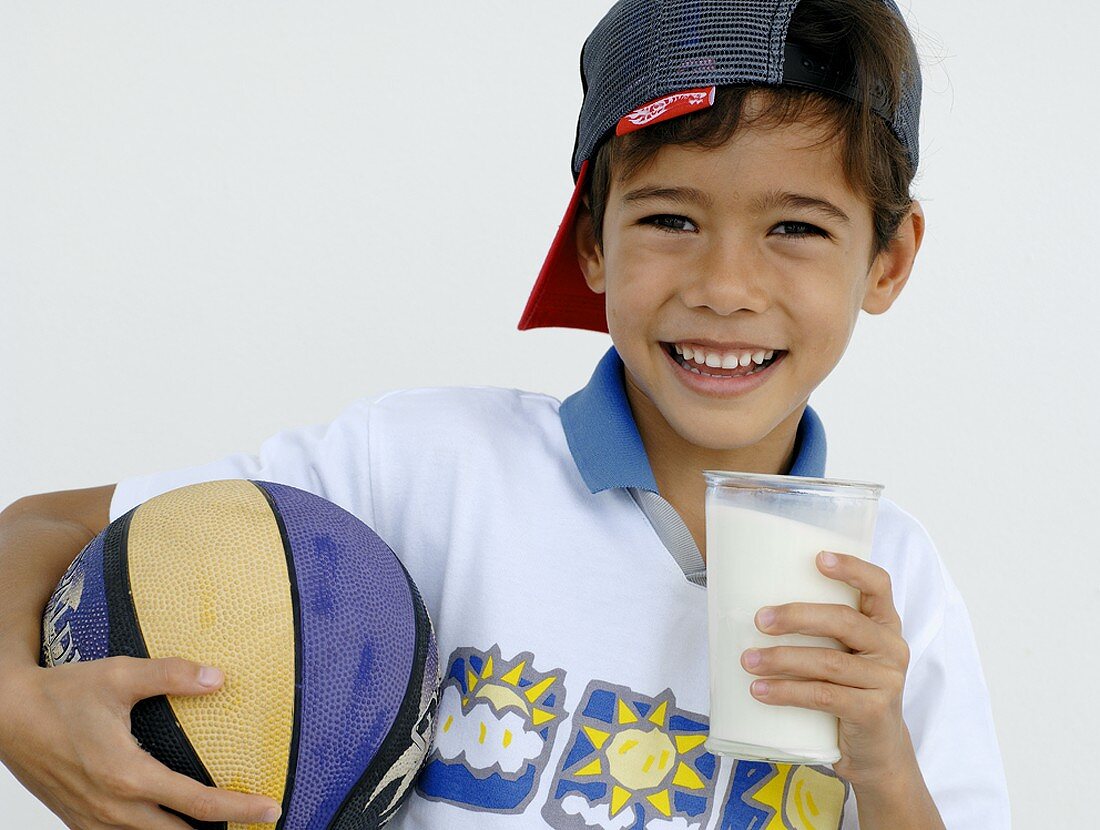 Junge hält ein Glas Milch und einen Ball in der Hand