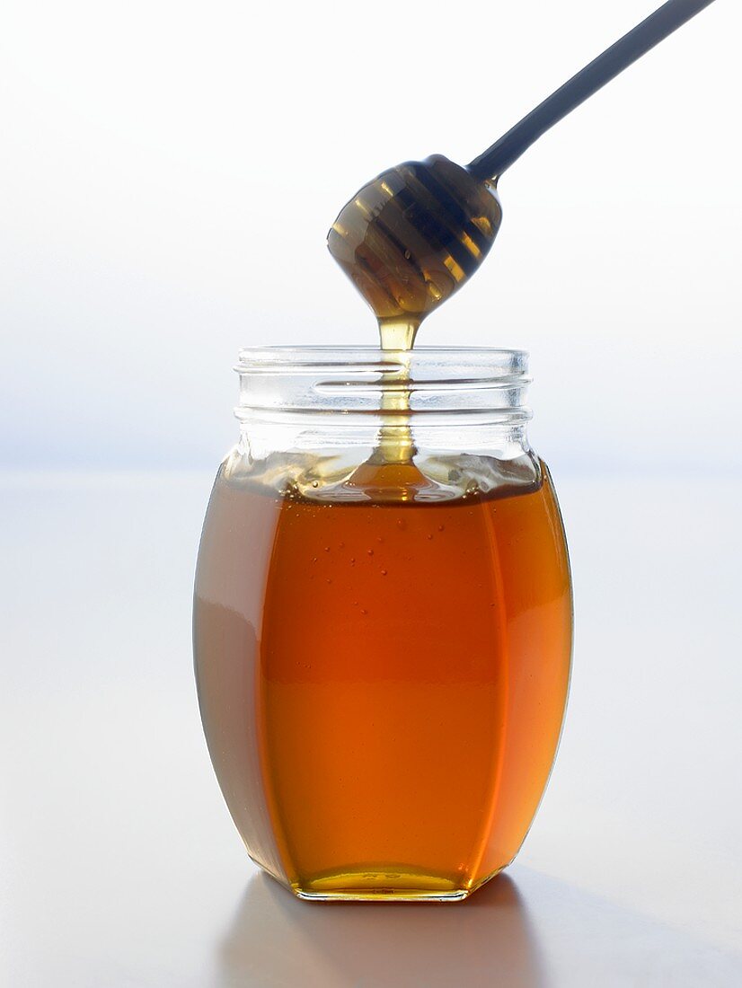 Honig fliesst vom Honiglöffel ins Glas