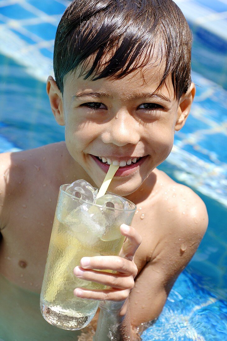 Junge trinkt ein Glas Eistee im Pool
