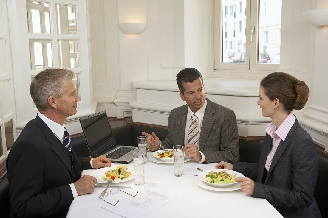 Zwei Männer sitzen mit Geschäftsfrau beim Essen