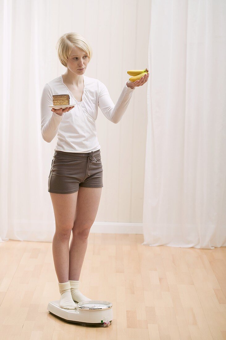 Junge Frau mit einem Stück Kuchen und Bananen auf der Waage