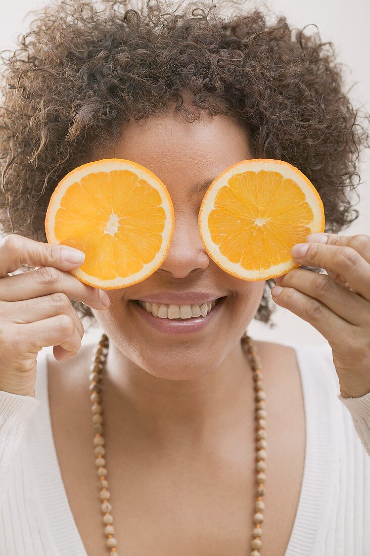 Young woman holding two orange slices in front of her face