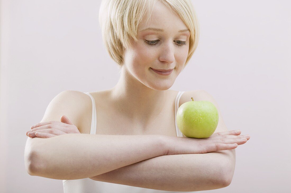 Young woman balancing an apple on folded arms